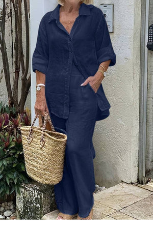Woman wearing navy relaxed shirt and trousers two-piece set with rolled sleeves and straw handbag outdoors