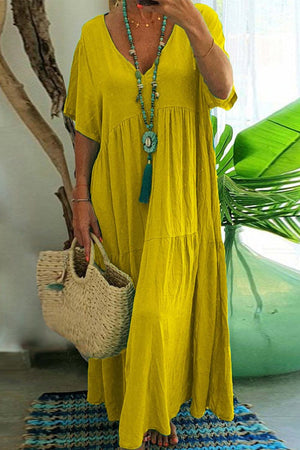 Yellow V-neck two-tiered maxi swing dress with loose sleeves and tiered flowing skirt, styled with a turquoise necklace and woven handbag.
