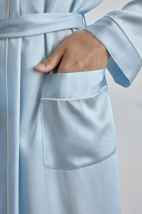 Close-up of hand in pocket of light blue Mulberry silk nightgown with sash belt and white piping detail