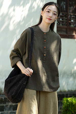 Woman wearing olive green ramie linen and cotton blouse with long sleeves and front buttons carrying black shoulder bag outdoors
