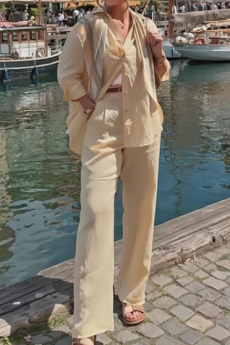Woman wearing beige linen blend two-piece set with loose pants and open shirt near marina dock