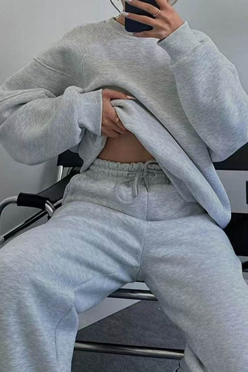 Woman wearing light gray comfy chic tracksuit with relaxed fit and long sleeves sitting on chair taking mirror selfie