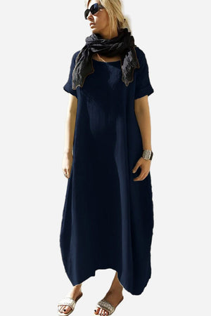 Woman wearing navy Breeze Cocoon Dress with rolled sleeves and deep pockets, styled with scarf and sandals