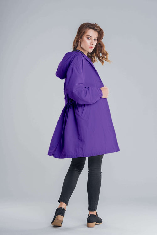 Water-resistant oversized windbreaker rain jacket in purple with hood, modeled by woman against gray background