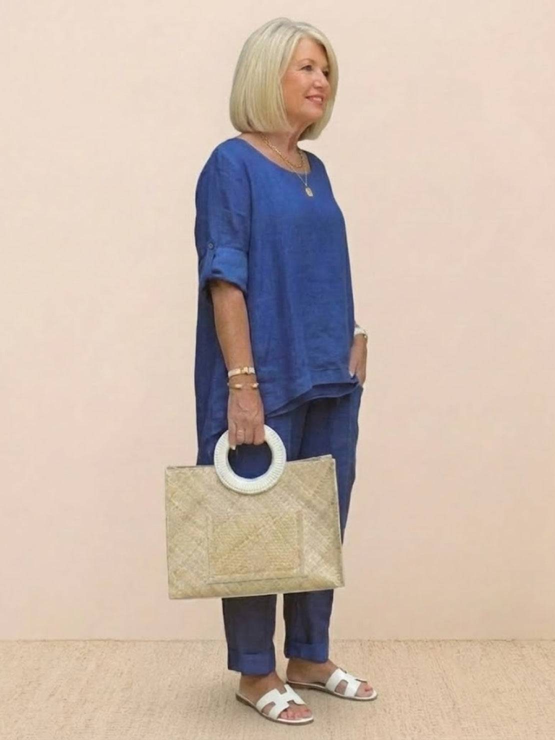 woman wearing royal blue asymmetrical two-piece trouser set with rolled sleeves and holding a beige woven handbag