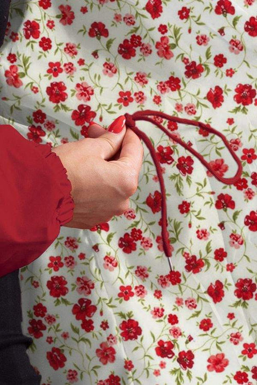 Close-up of hand adjusting red drawstring on Rain Couture Windbreaker sleeve against floral background