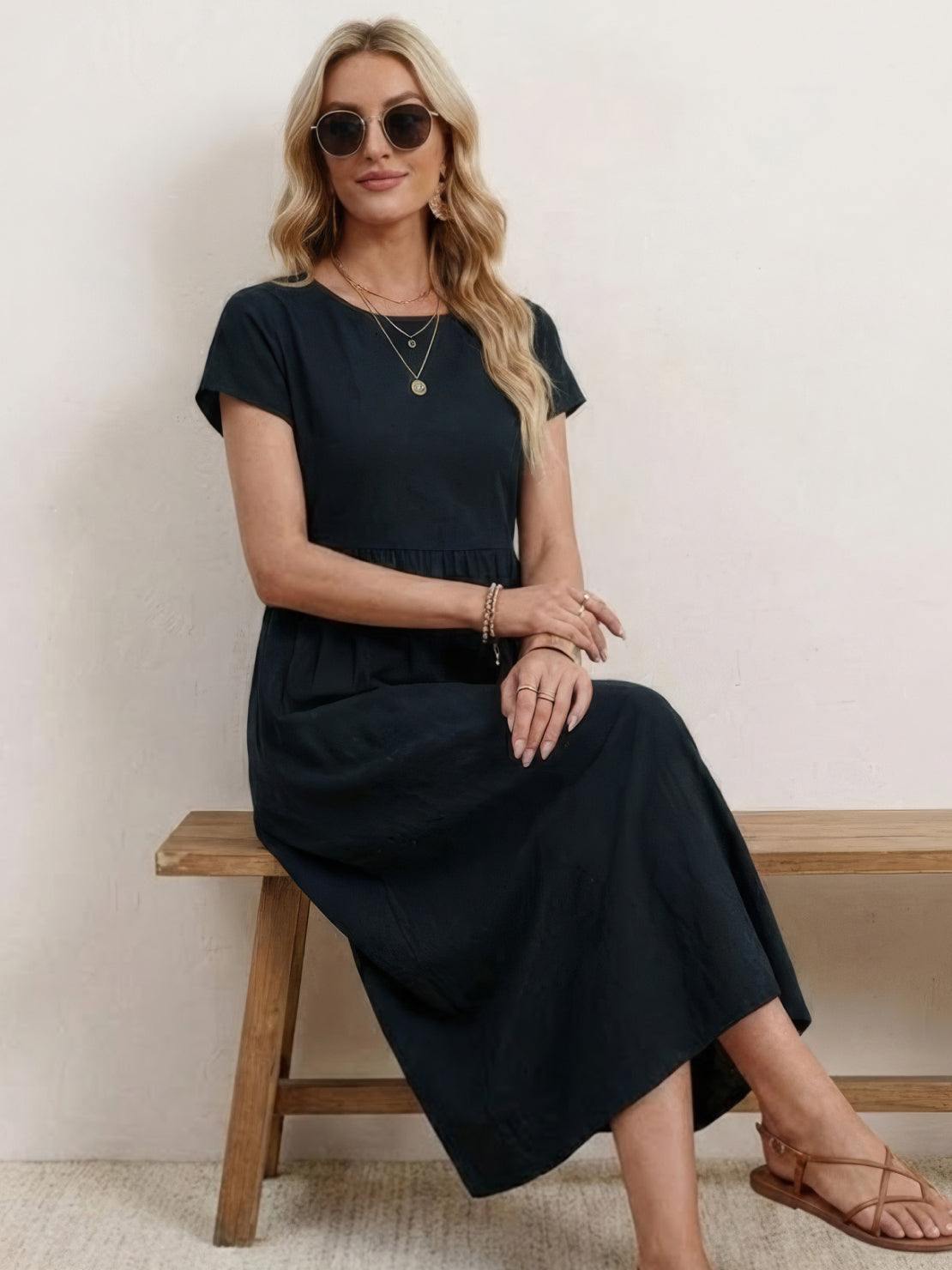 Woman wearing a capped-sleeve voluminous pleated midi dress with pockets and flowing stomach-flattening drape