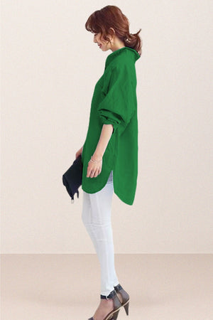 Woman wearing oversized green linen shirt with rolled sleeves and white pants, holding a black clutch.