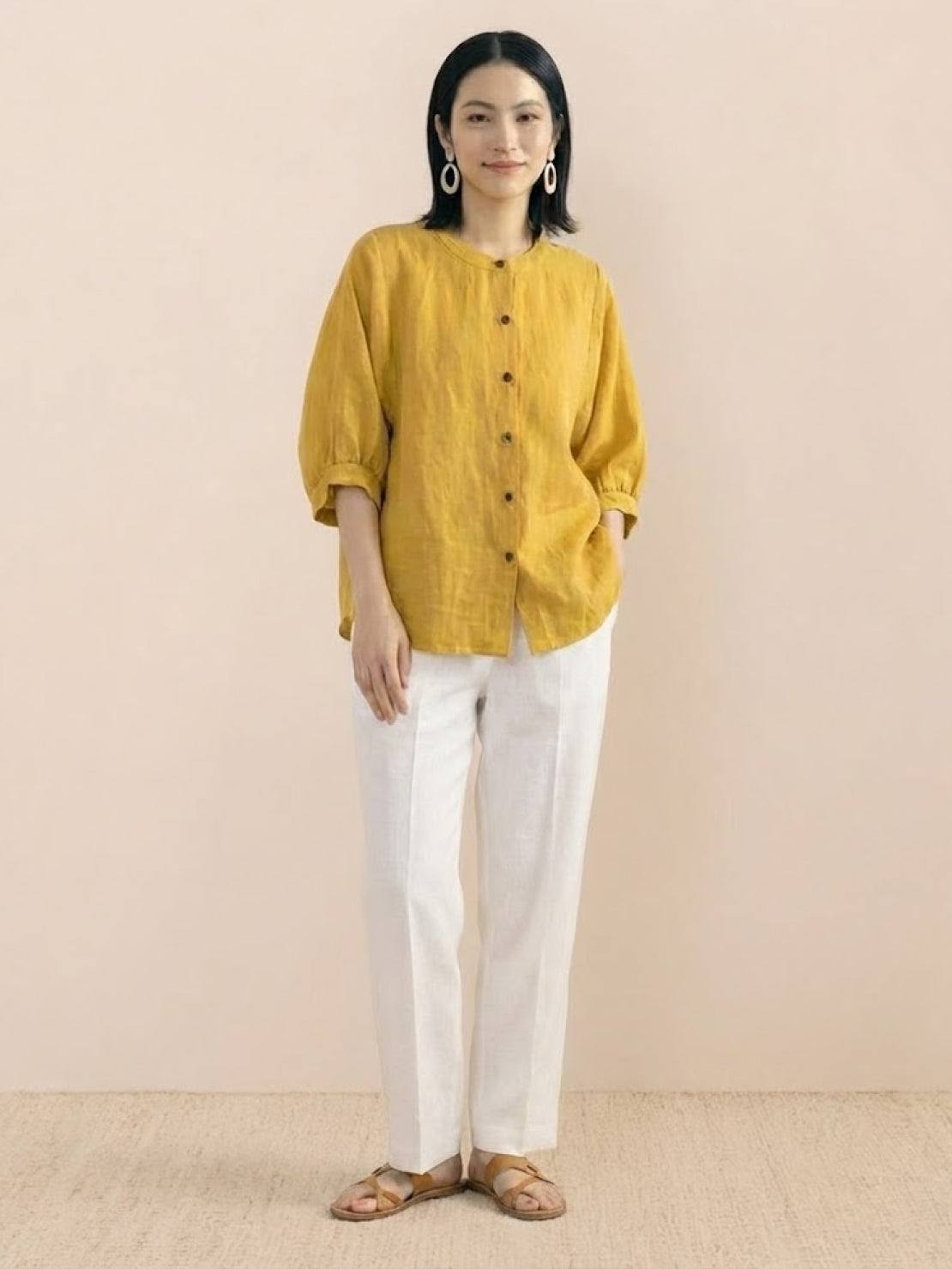 Relaxed loose breathable linen blouse in mustard yellow with button-down front and three-quarter sleeves, styled with white pants and sandals