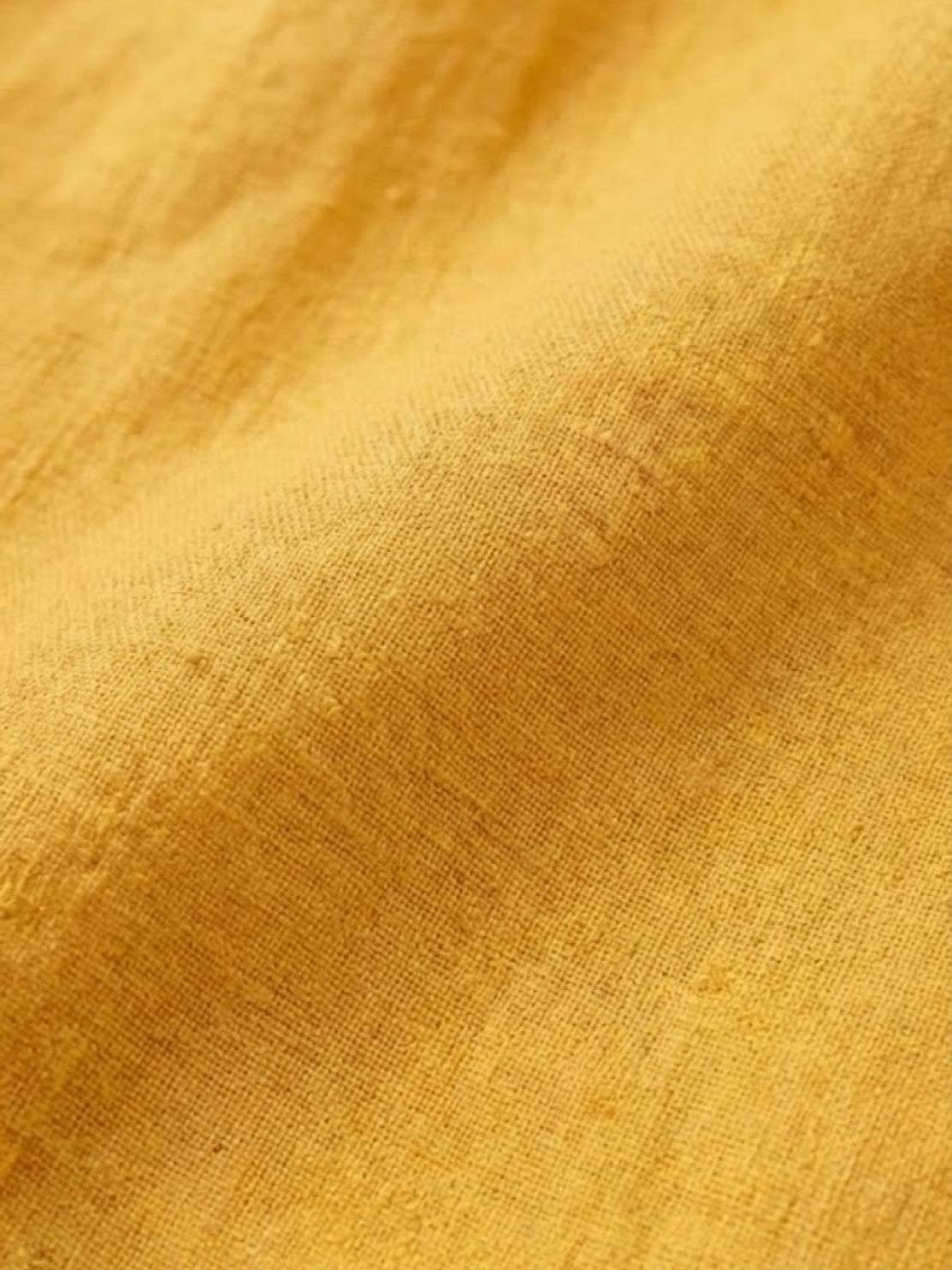 close-up of relaxed loose breathable linen fabric in warm yellow color