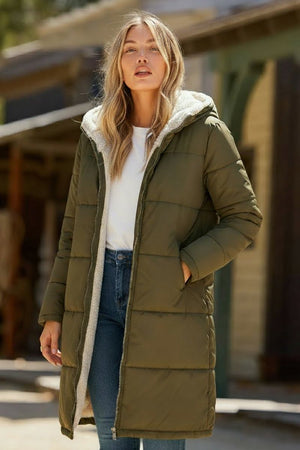 Woman wearing olive green Sherpa-lined hooded teddy coat with plush interior and long puffer style outdoors