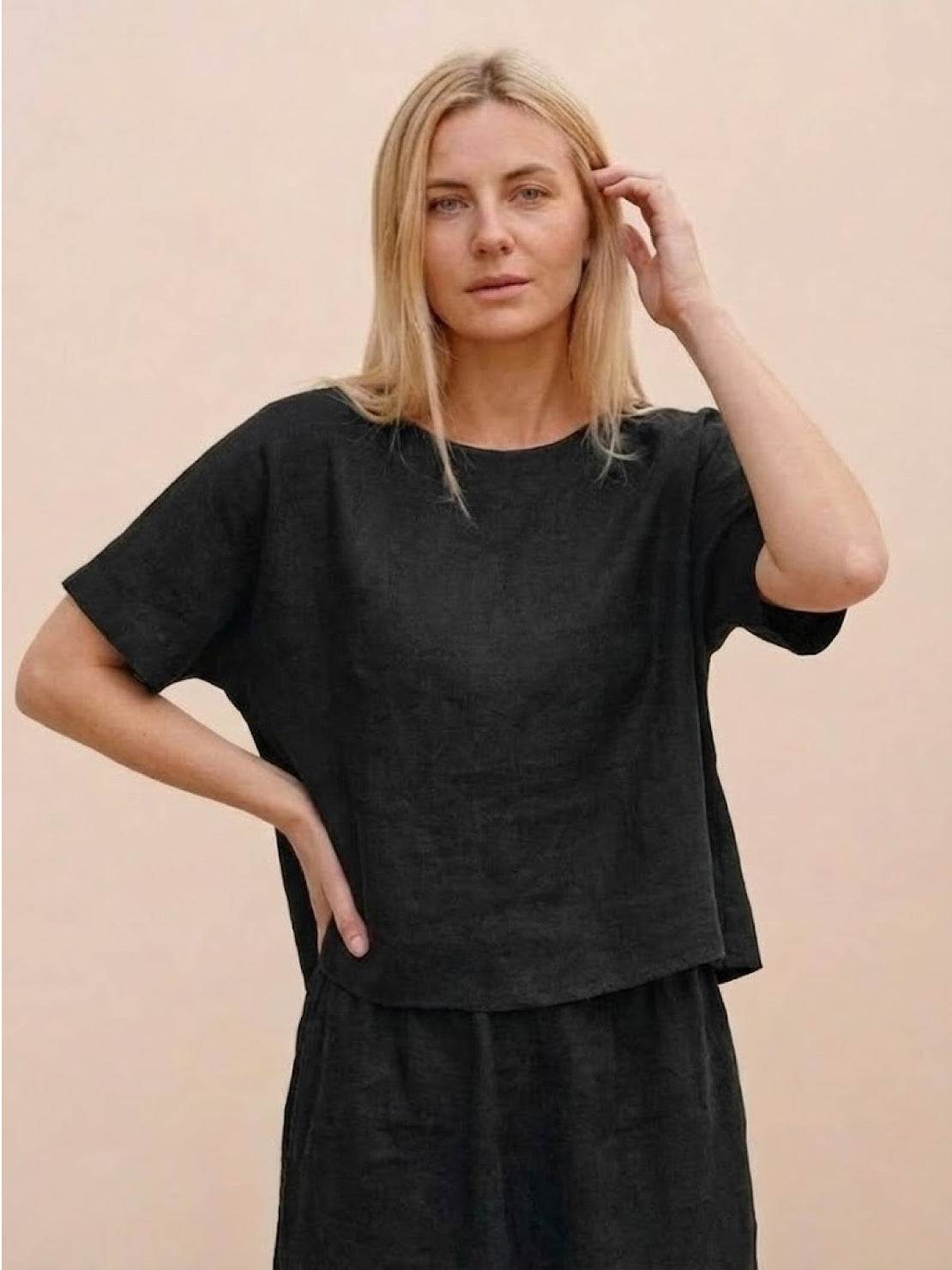 woman wearing black loose fit co-ord set with relaxed short sleeves and wide-leg pants against neutral background