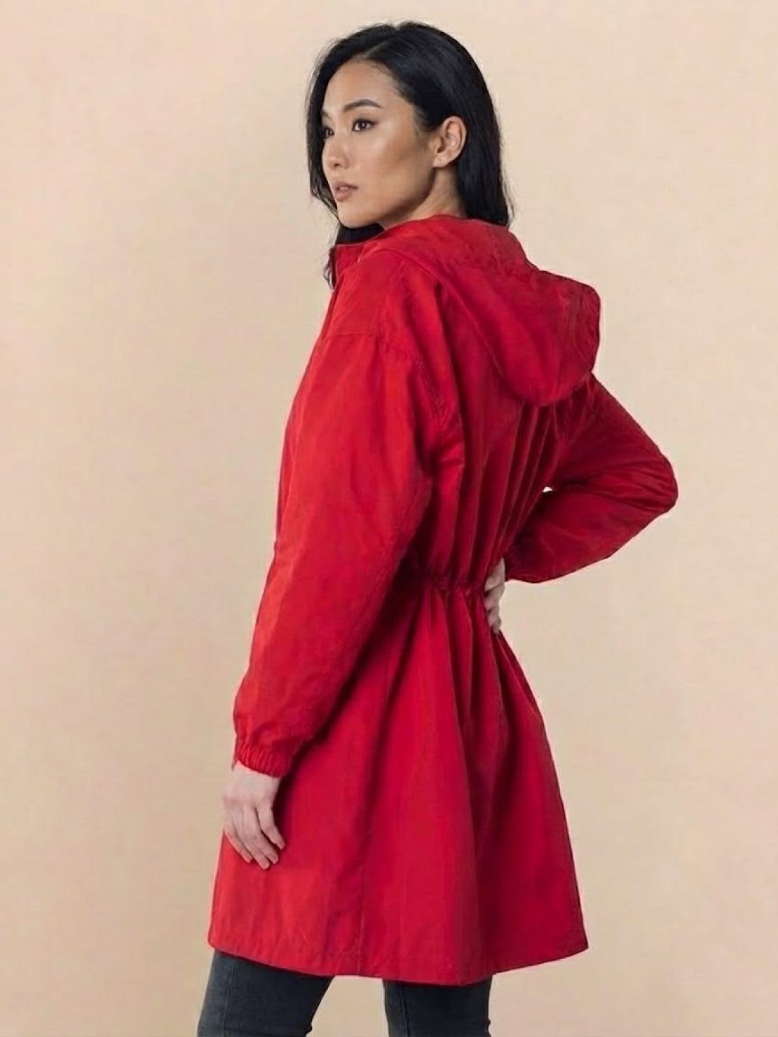 Woman wearing red Rain Couture Windbreaker with hood, oversized fit, and adjustable waist on beige background