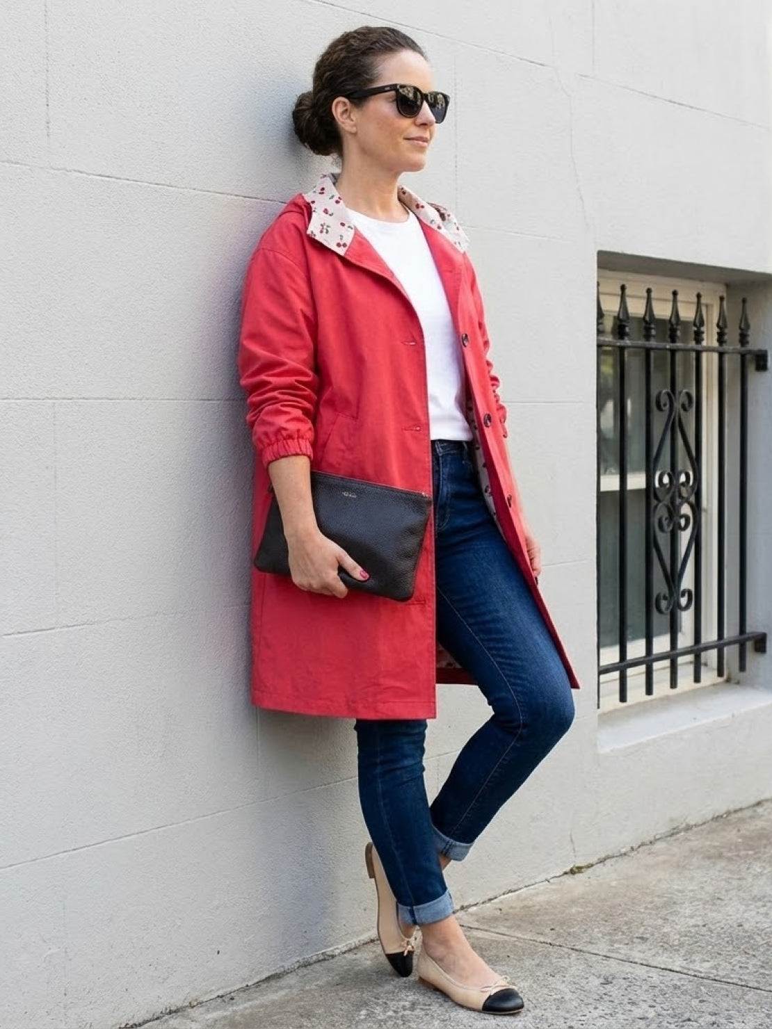 Woman wearing a red oversized Rain Couture Windbreaker with jeans and flats, standing against a wall outdoors