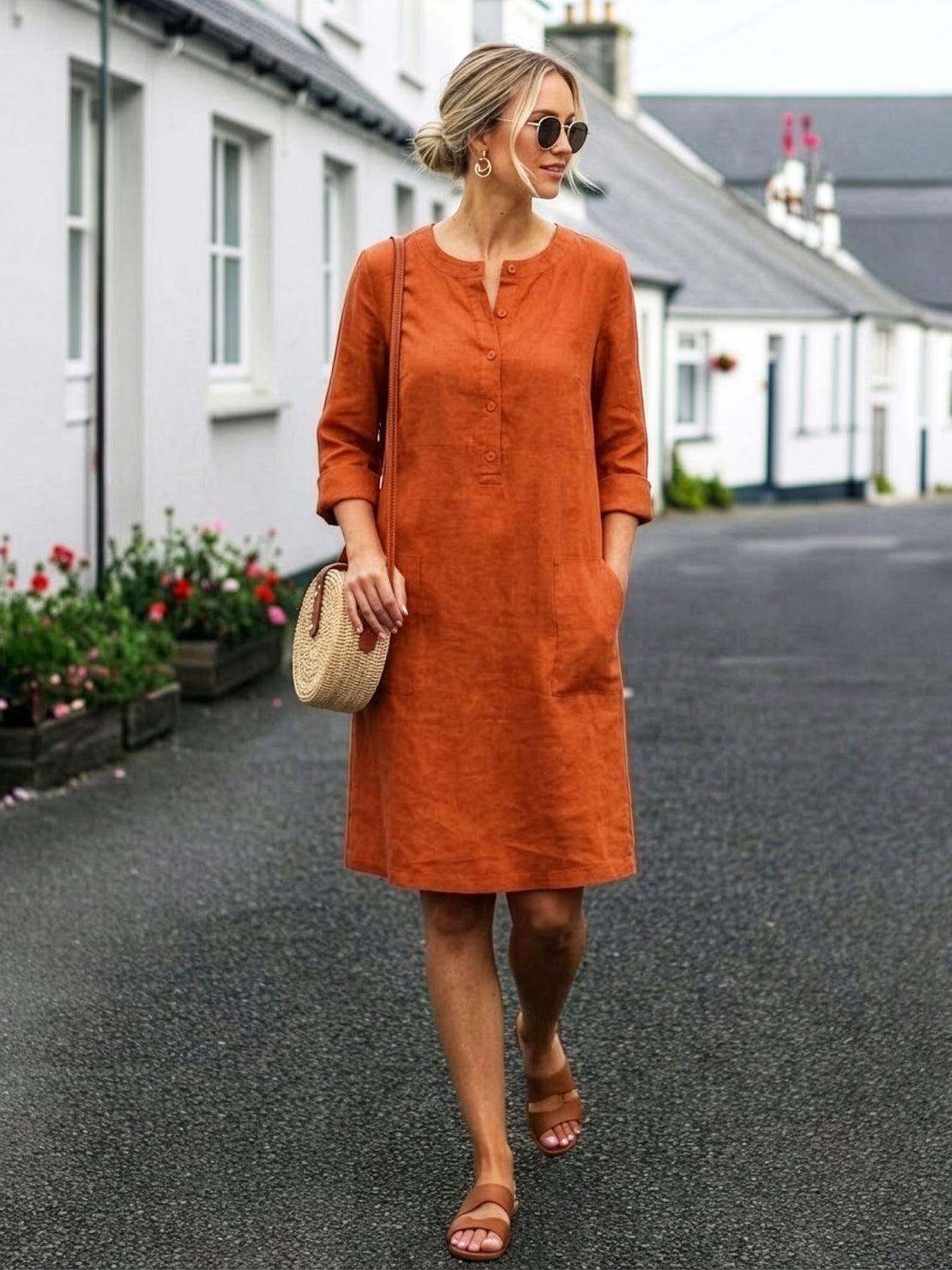 woman wearing rust-colored casual cotton dress with rolled 3/4 sleeves and pockets walking outdoors