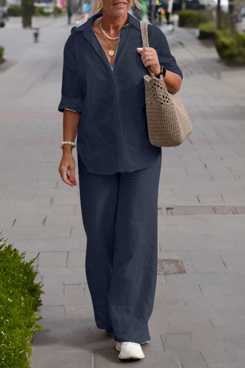 Woman wearing a relaxed shirt and trousers two-piece set in dark color walking outdoors with a handbag and white shoes.