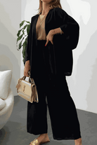 Woman wearing black Chic Comfort Kimono two-piece set with beige top and beige handbag, indoor setting