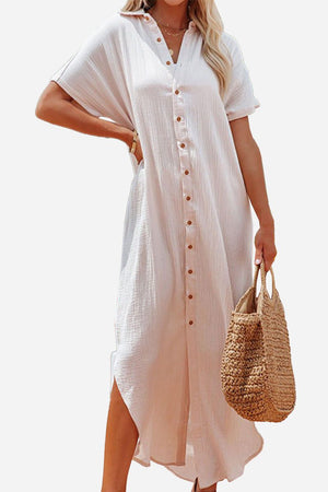 Woman wearing a light pink full-length button-down beach cover-up dress holding a woven straw bag.