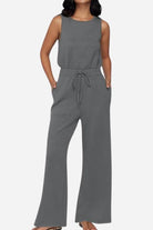 Woman wearing a gray sleeveless wide leg pants jumpsuit with drawstring waist and pockets