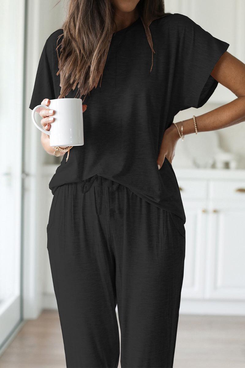 Woman wearing black ultra-soft two-piece loungewear set with batwing sleeves and jogger pants holding a white mug indoors