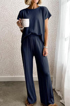 Woman wearing navy blue First Class Travel two-piece set with pleated wide-leg pants holding a mug indoors