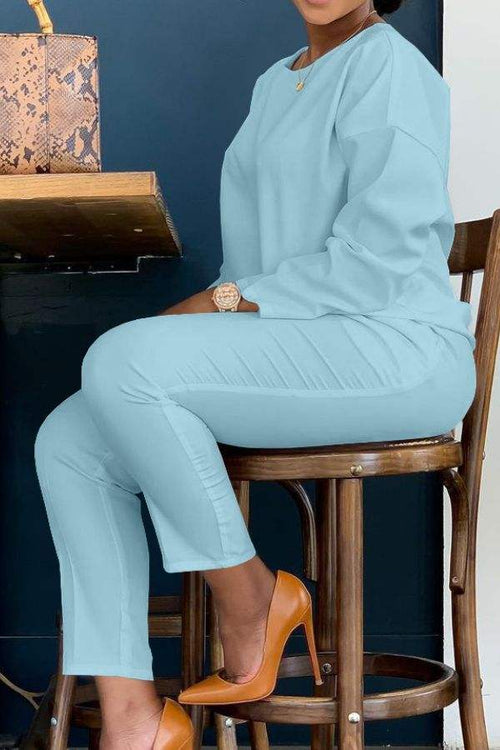 Woman wearing light blue cotton two-piece set vibrant outfit sitting on wooden chair with brown heels and handbag on table