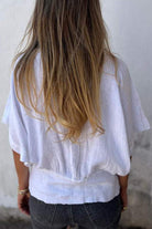Back view of woman wearing white pure linen short-sleeve blouse with relaxed fit and natural wrinkles, paired with dark jeans.