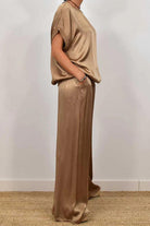 Woman wearing a beige Silken Escape Satin Two-Piece Set with loose-fitting top and wide-leg pants.