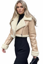 Woman wearing a beige cropped faux leather sherpa jacket with cream trim and black pants