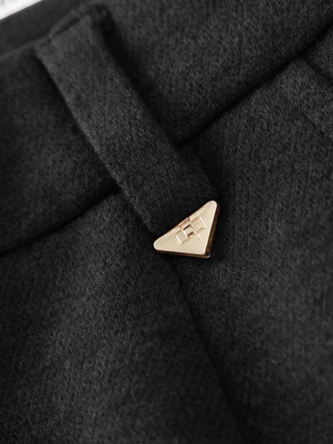 Close-up of black thermal wool blend trousers with gold triangular button and textured fabric detail