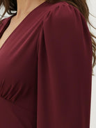 Woman wearing slimming V-neck midi dress with button-front and ruffle cuffs standing indoors