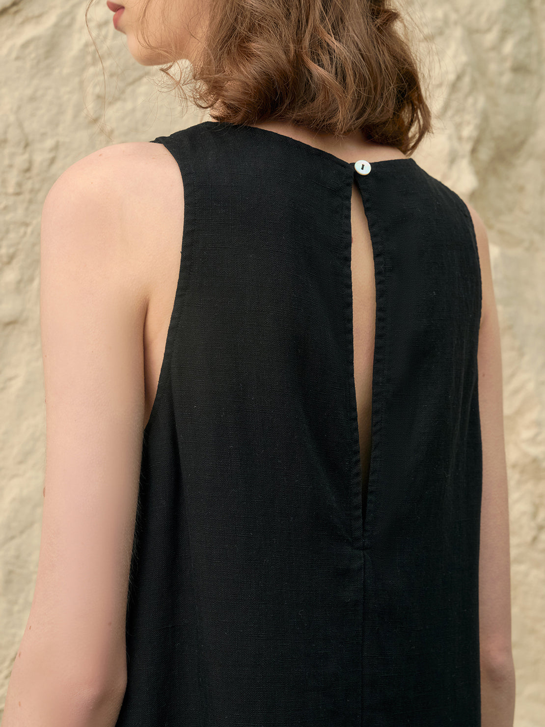 Woman wearing a sleeveless linen lyocell blend shift dress with hand-stitched neckline detail in white
