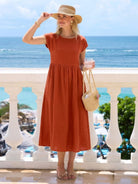 Woman wearing a capped-sleeve voluminous pleated midi dress with pockets and flowing skirt