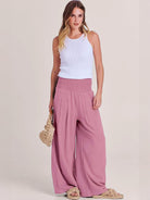 woman wearing pink high-waist palazzo pants with white sleeveless top and sandals carrying woven handbag