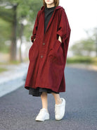 Oversized water-resistant windbreaker jacket with attached hood and large pockets in deep red, worn outdoors with white sneakers.