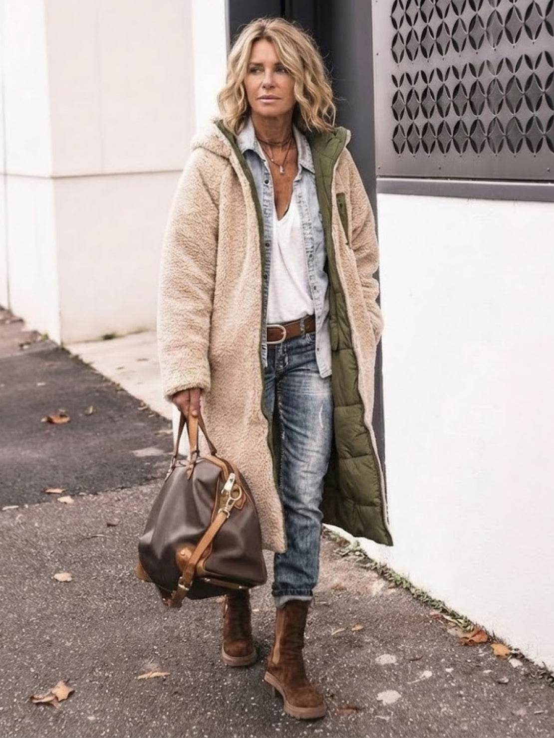 Woman wearing beige sherpa-lined hooded teddy coat with green lining, paired with denim jeans and brown boots, carrying brown handbag walking outdoors