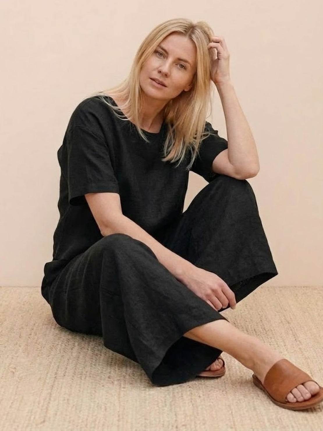 Woman wearing black loose fit co-ord set with wide-leg bottoms and relaxed short-sleeve top sitting on a beige rug