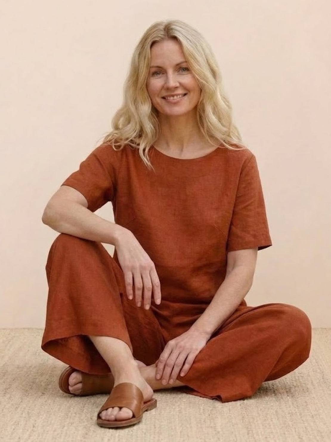 Woman wearing rust-colored loose fit co-ord set with short sleeves and wide-leg pants sitting on floor