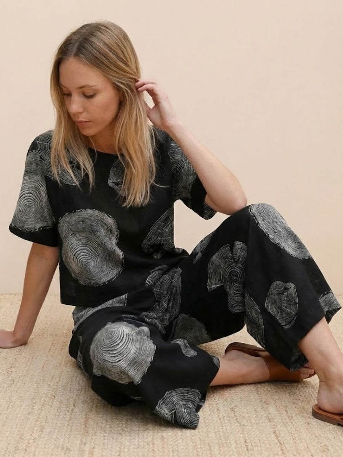 Woman wearing black and gray floral print loose fit co-ord set with short sleeves and wide-leg pants sitting on floor