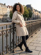 Woman wearing beige Rain Couture Windbreaker leaning on railing outdoors in city setting